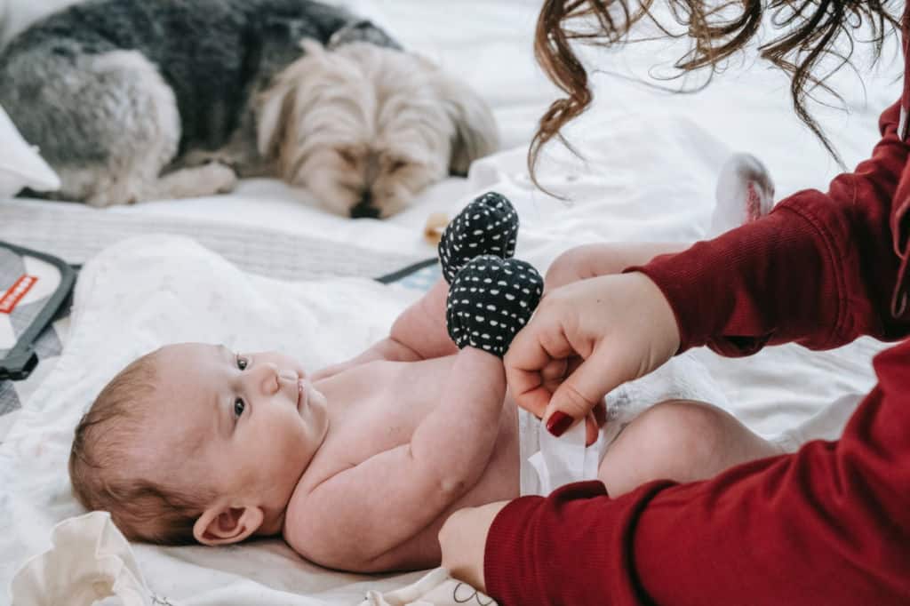 mother changing diaper for newborn baby next to dog