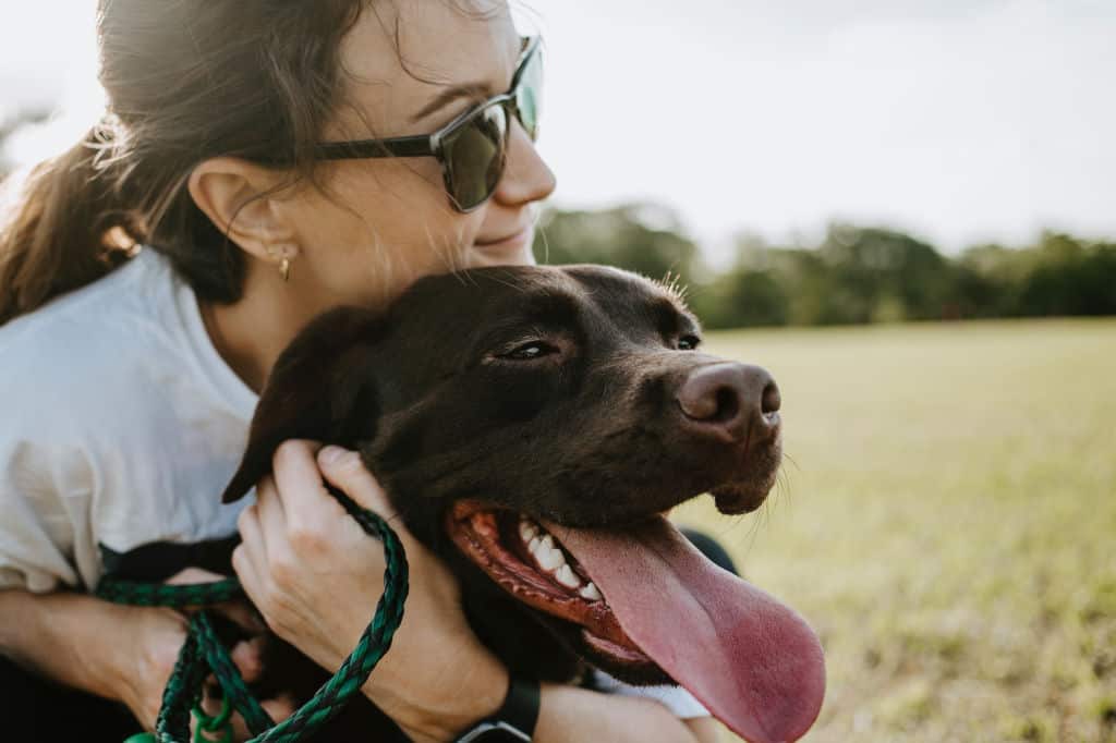 woman hugging a black dog in the field