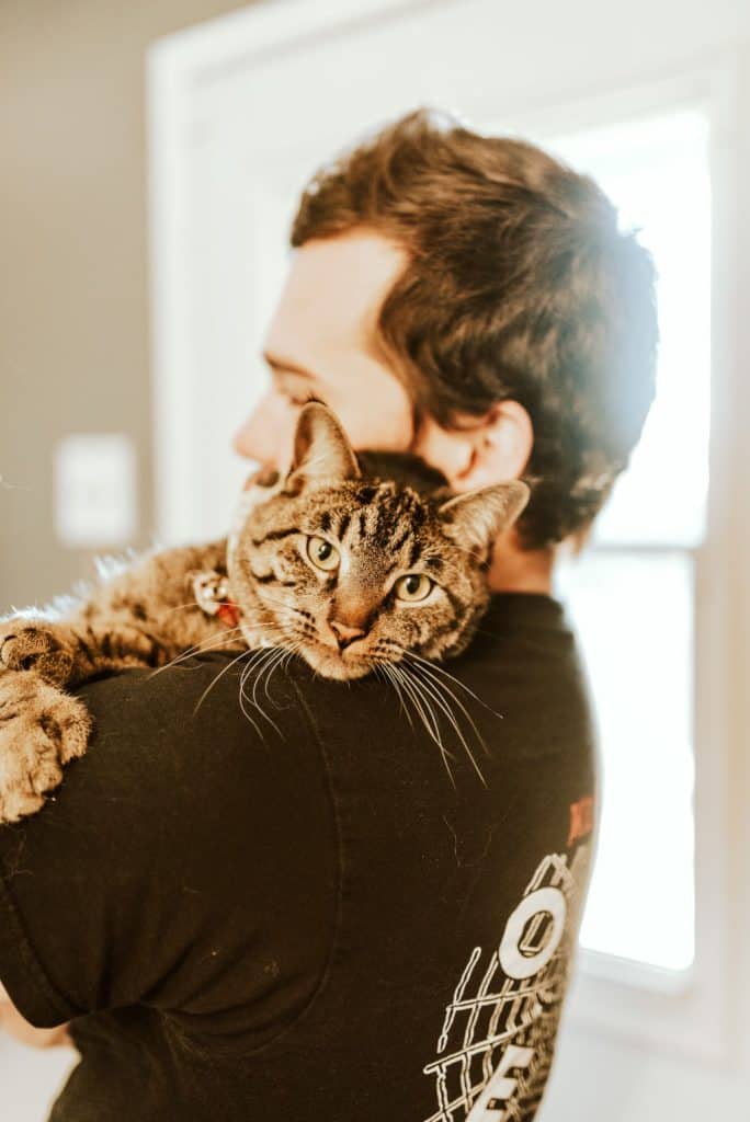 man holding brown striped cat on his shoulder