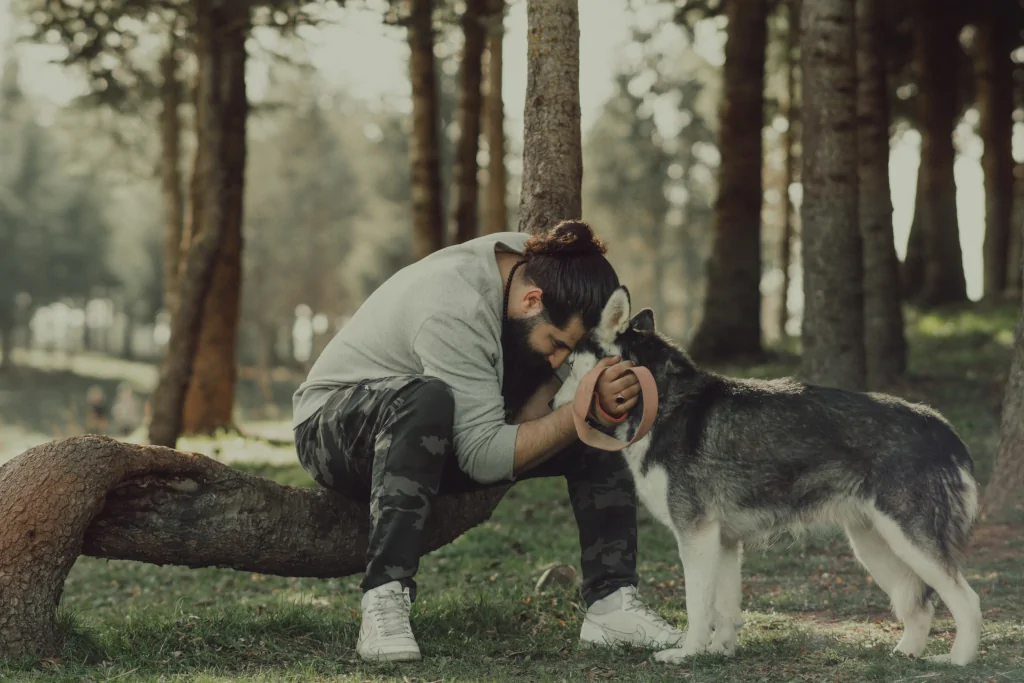 man hugging a siberian husky in the park near trees