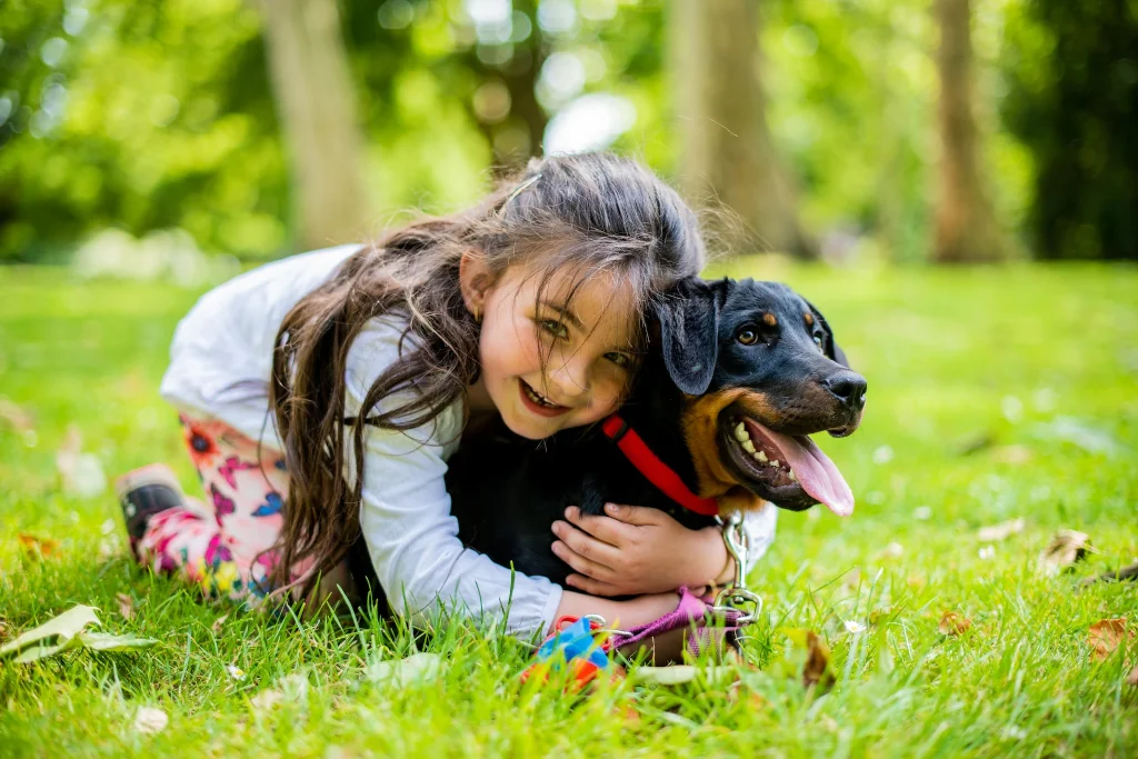 little girl hugging a black dog on the grass
